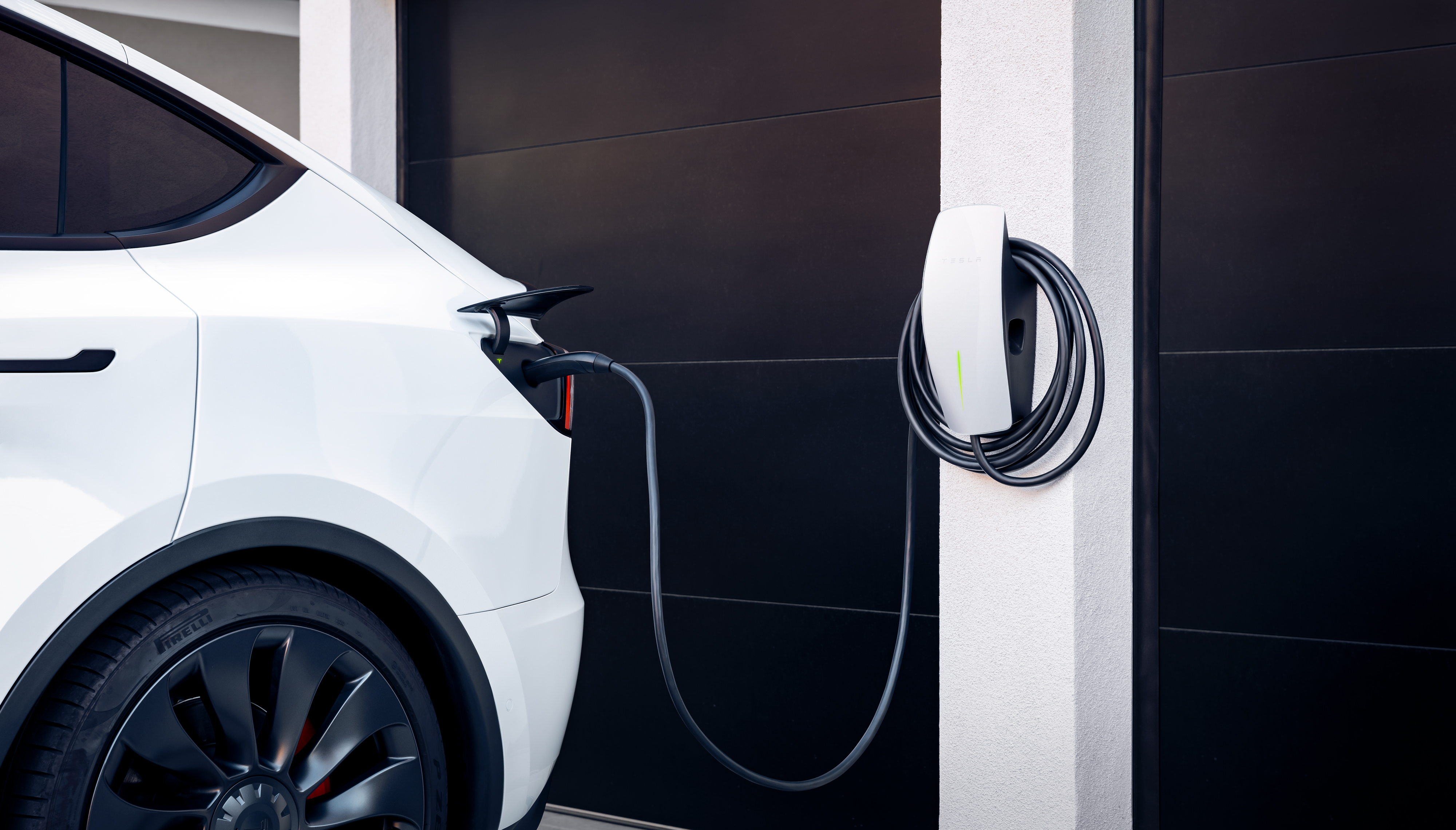 White Tesla plugged into Wall Connector at home garage